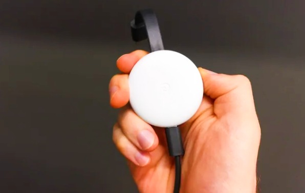 a person  holds a Chromecast device in his hands its color is white and black